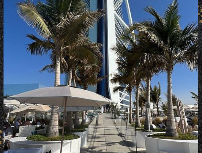 The Burj Al Arab hotel in Dubai, a stunning architectural marvel, stands tall on a beautiful sunny day amidst palm trees.